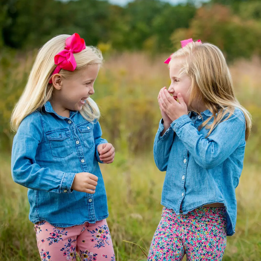 Two little girls standing in a field and one girl is covering her mouth.